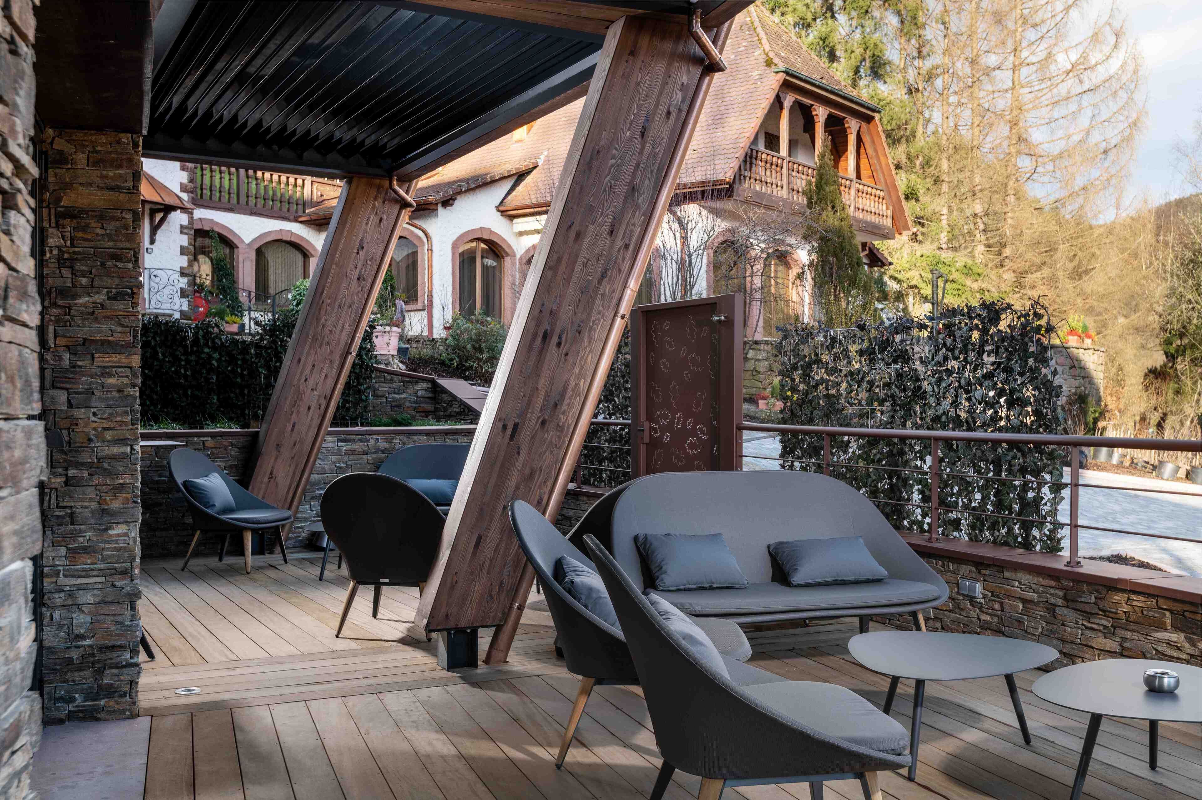 A wooden deck with outdoor seating, stone walls, and a view of a river.