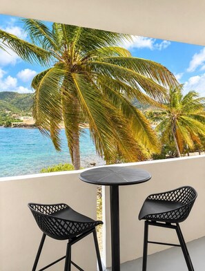 A balcony with a round table and two chairs, overlooking a beach with palm trees and a clear blue sea. - Hotel on the Cay (Christiansted)