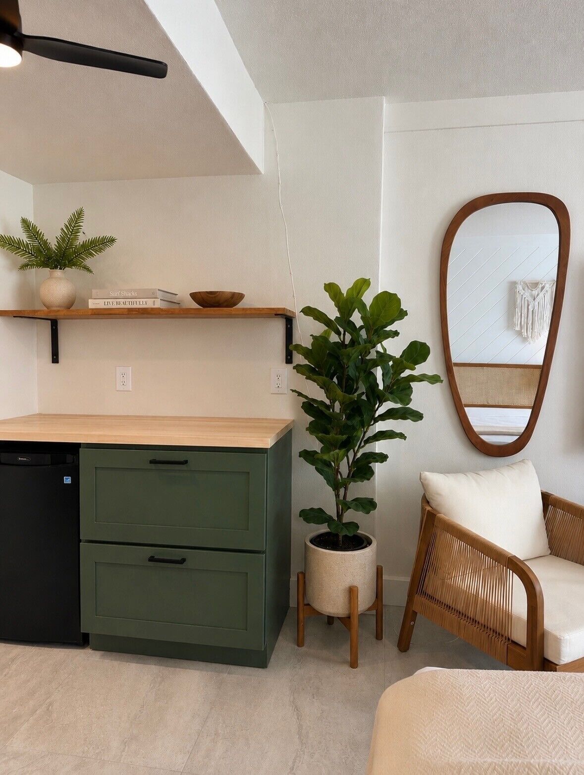 A kitchen with a green cabinet, a wooden countertop, a potted plant, a wicker chair, and a mirror on the wall.
