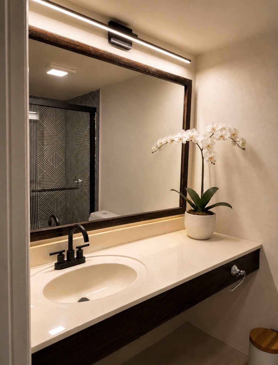 A bathroom with a white sink, a black faucet, a mirror with a wooden frame, and a potted orchid.