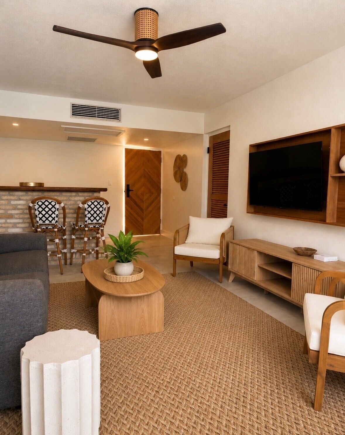 A modern living room with a ceiling fan, a TV mounted on the wall, a sofa, a coffee table, and a dining area with chairs.