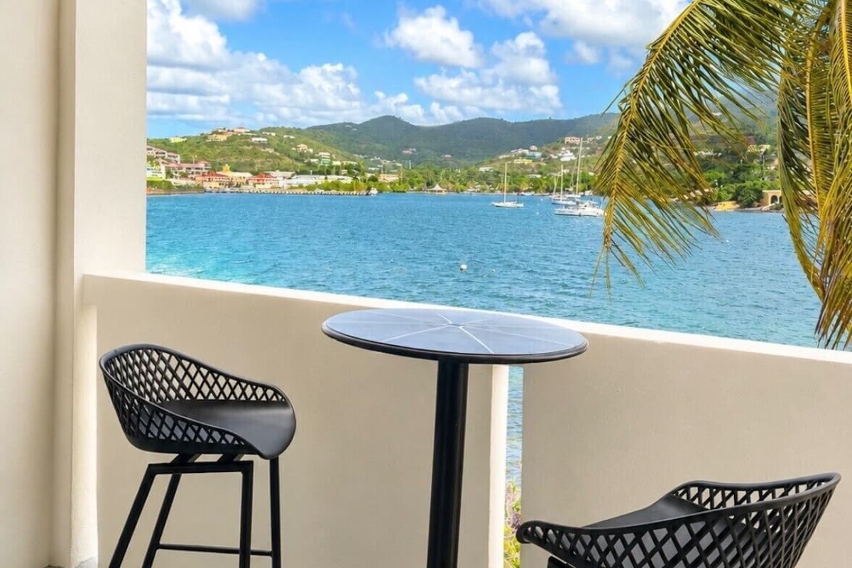 Ein Balkon mit zwei schwarzen Stühlen und einem kleinen runden Tisch, mit Blick auf ein Gewässer mit Booten und einer Stadt in der Ferne.