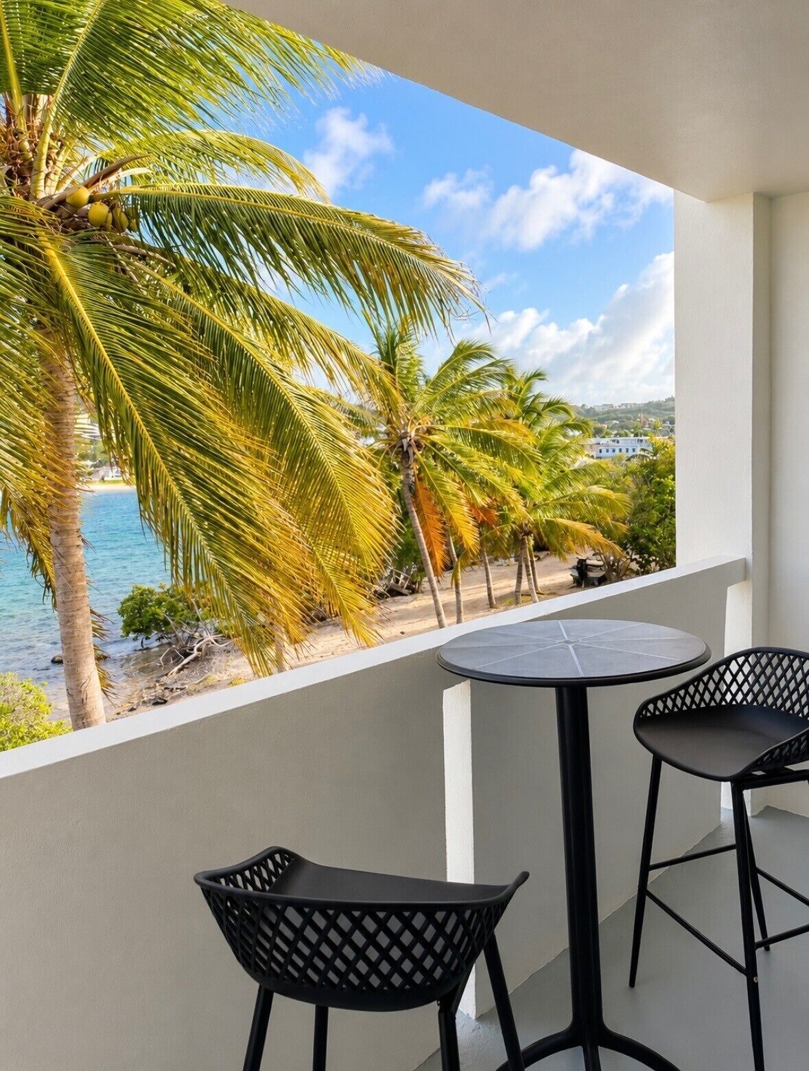 Ein Balkon mit Blick auf das Meer, Palmen und ein weißes Gebäude in der Ferne.