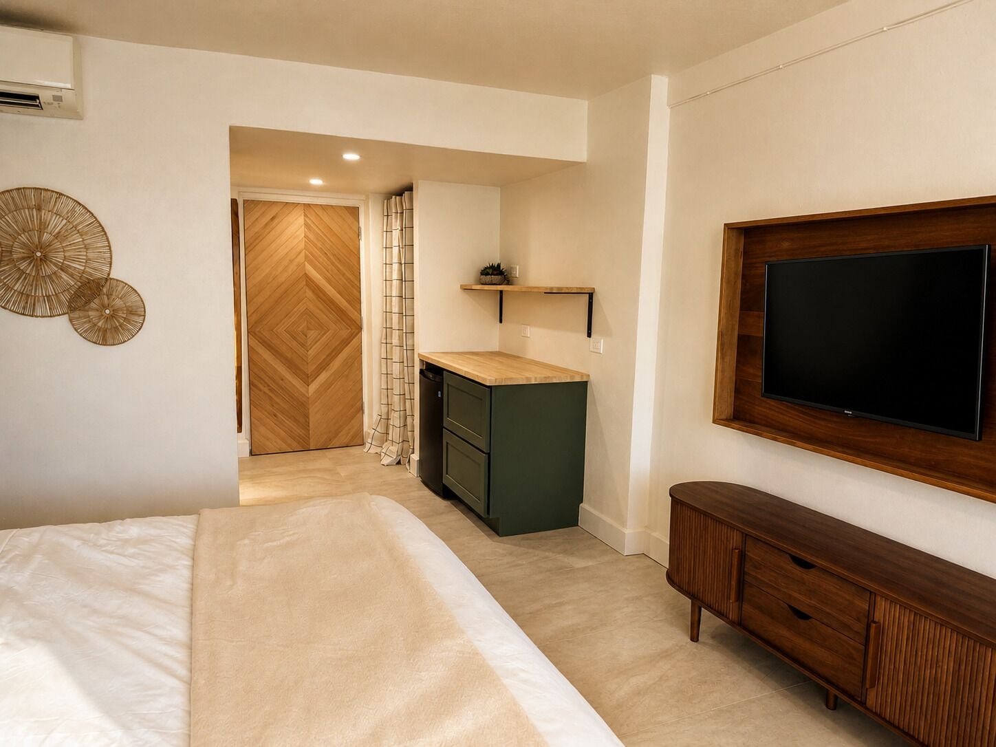 A modern bedroom with a bed, a TV, a wooden cabinet, and a kitchen area.