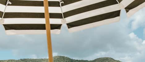 A beach scene with a striped umbrella, a boat, and buildings in the background.