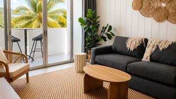 Een moderne woonkamer met een bank, salontafel en stoelen, een groot raam met uitzicht op palmbomen, en een plafondventilator.