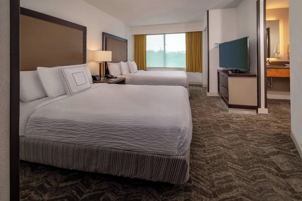 A hotel room with two beds, a TV, a desk, and a bathroom with a mirror.