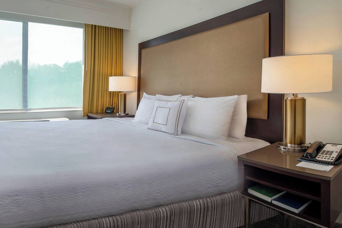 A hotel room with a large bed, two bedside lamps, a nightstand with a phone, and a window with curtains.