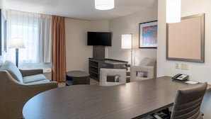 Ett hotellrum med ett stort konferensbord, två fåtöljer, en soffa, en tv och en tavla på väggen.