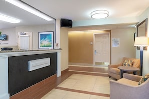 Un espace d’accueil d’hôtel comprenant un comptoir de réception, un téléviseur fixé au mur, un tableau encadré et un panneau indiquant les numéros de chambre.