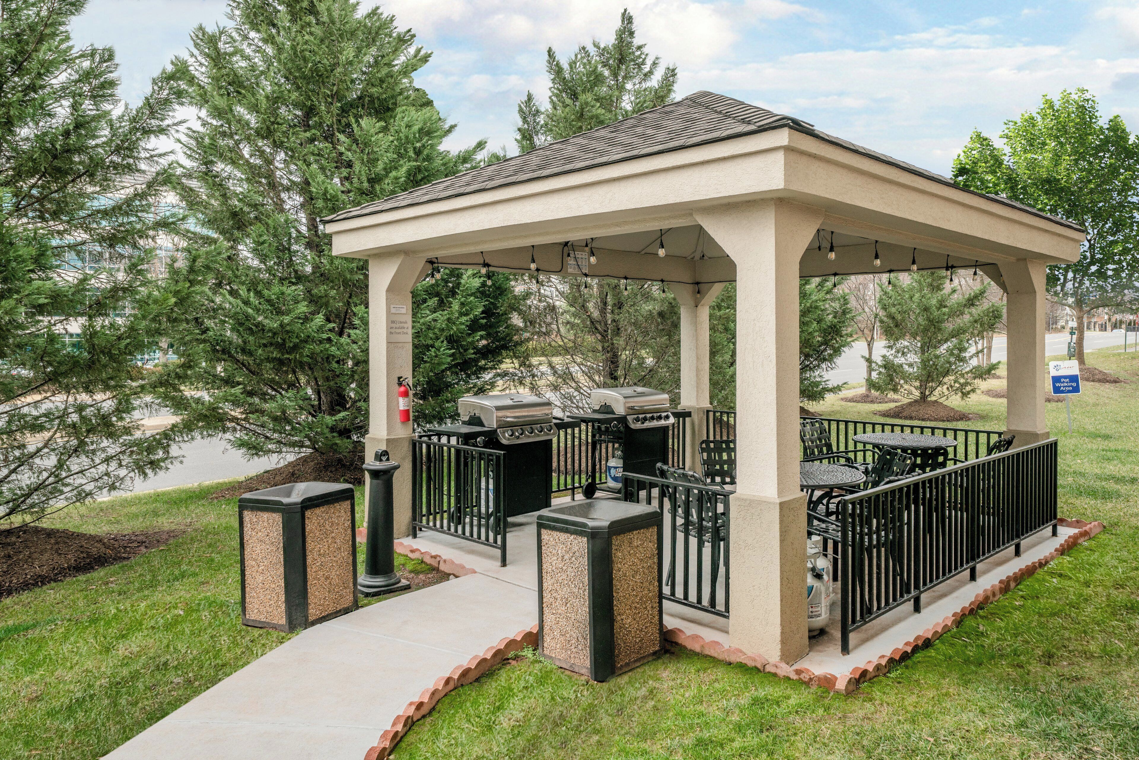A covered outdoor area with a grill and seating, surrounded by trees and a walking area sign.