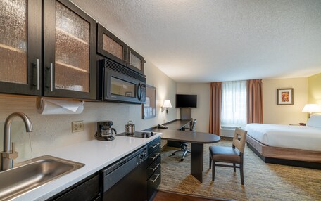 A hotel room with a kitchenette, a bed, a desk, and a chair.