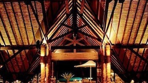 An indoor dining area with tables set for meals, wooden beams on the ceiling, and a central light fixture.