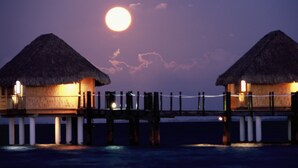 Two thatched-roof overwater bungalows connected by a wooden deck.