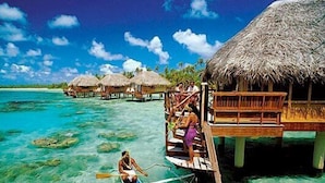 A clear turquoise sea with overwater bungalows and a person paddling a canoe.