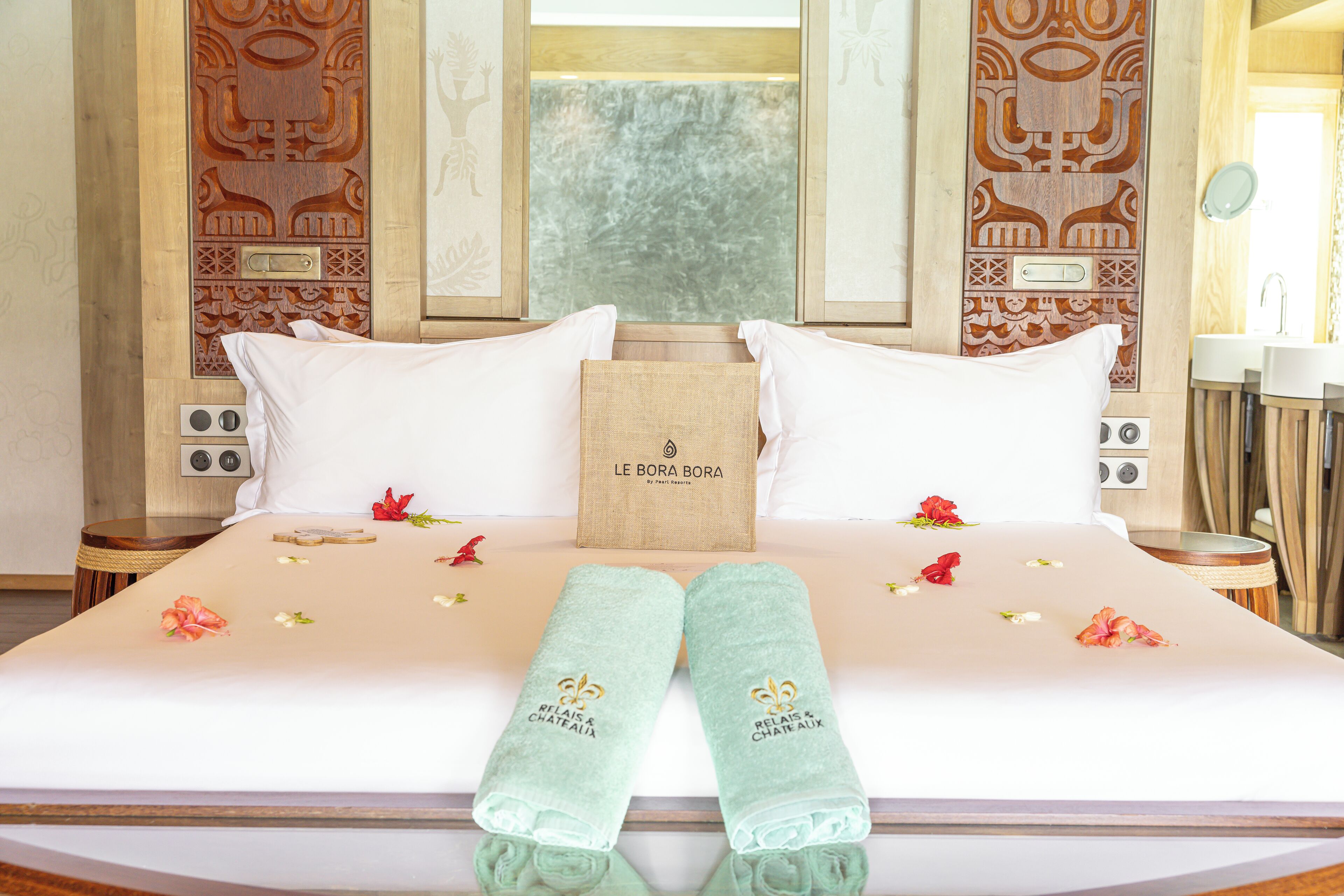A hotel room with a bed, pillows, a wooden headboard, a small table, and a wall with decorative panels.