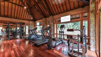 Un gimnasio con cintas de correr, elípticas y equipo de pesas, con piso de madera y paredes de piedra.