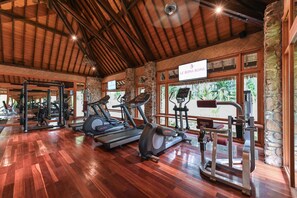 A gym with treadmills, elliptical machines, and weight equipment, featuring a wooden floor and stone walls.