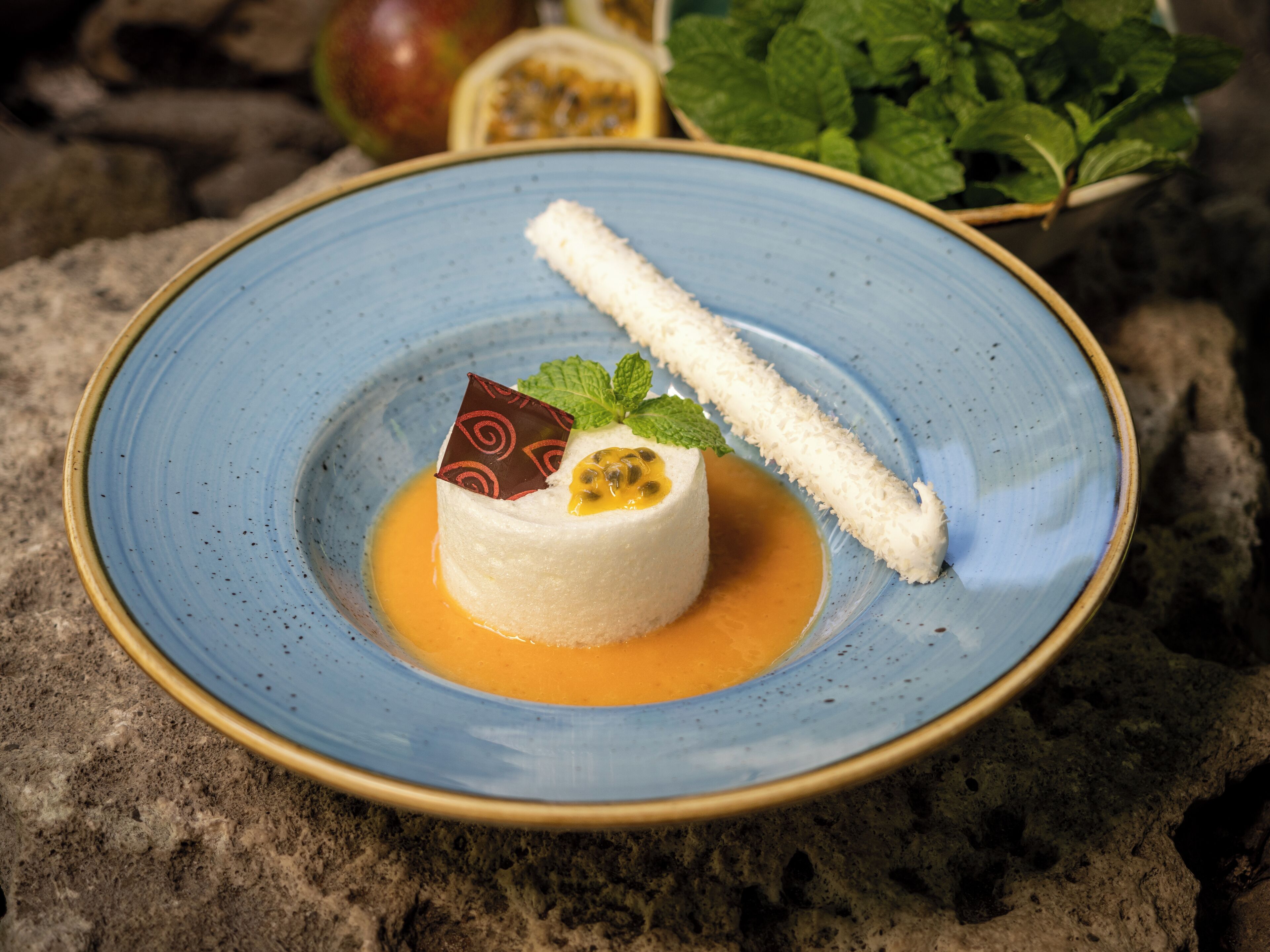 Dessert auf blauem Teller mit Karamellsauce, ein Stück weißer Kuchen und ein Minzblatt als Garnitur.