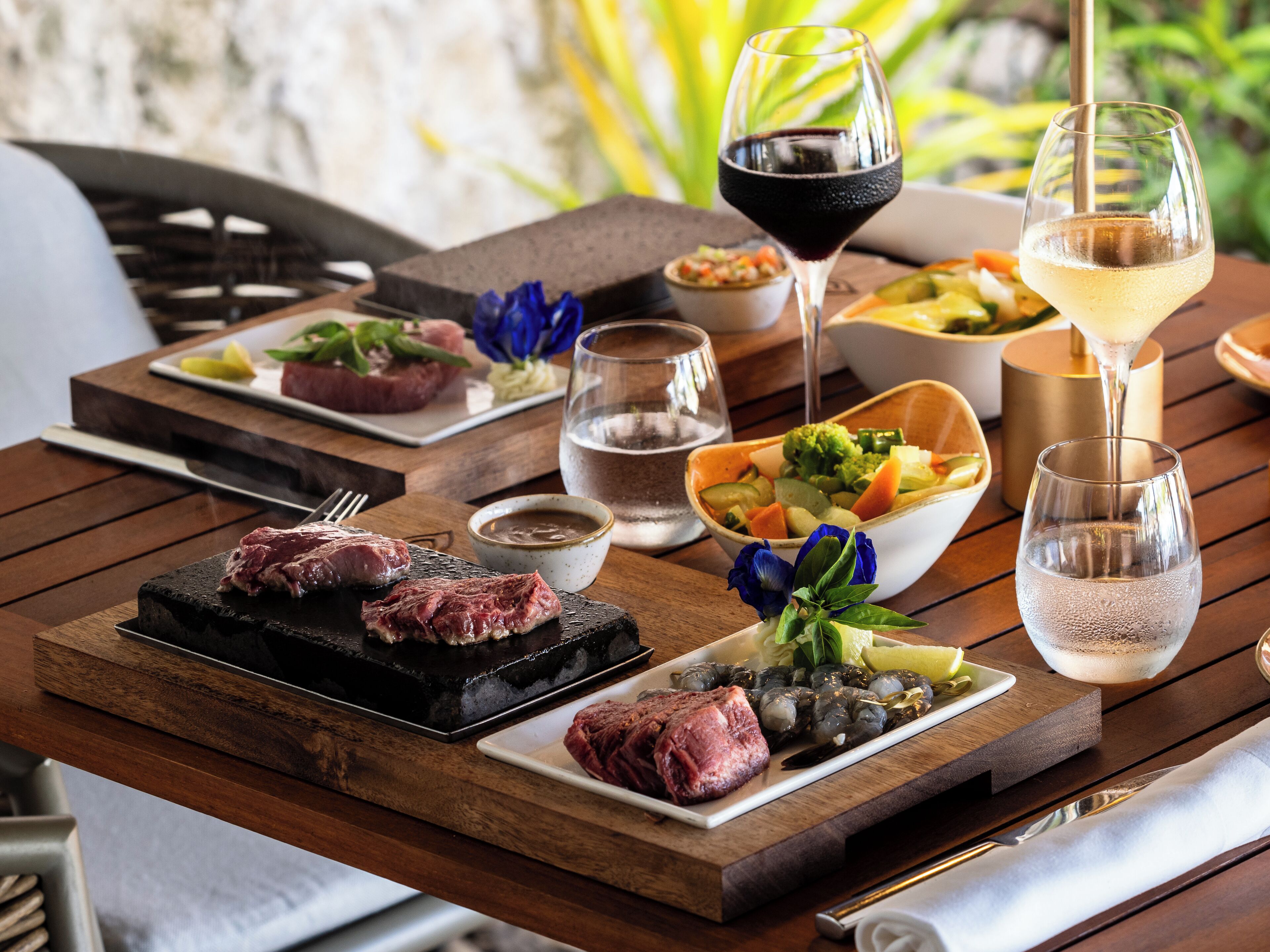 Ein Holztisch mit einer Auswahl an Speisen, darunter gegrilltes Fleisch, Salate und Getränke.