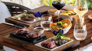 Ein Holztisch mit einer Auswahl an Speisen, darunter gegrilltes Fleisch, Salate und Getränke.
