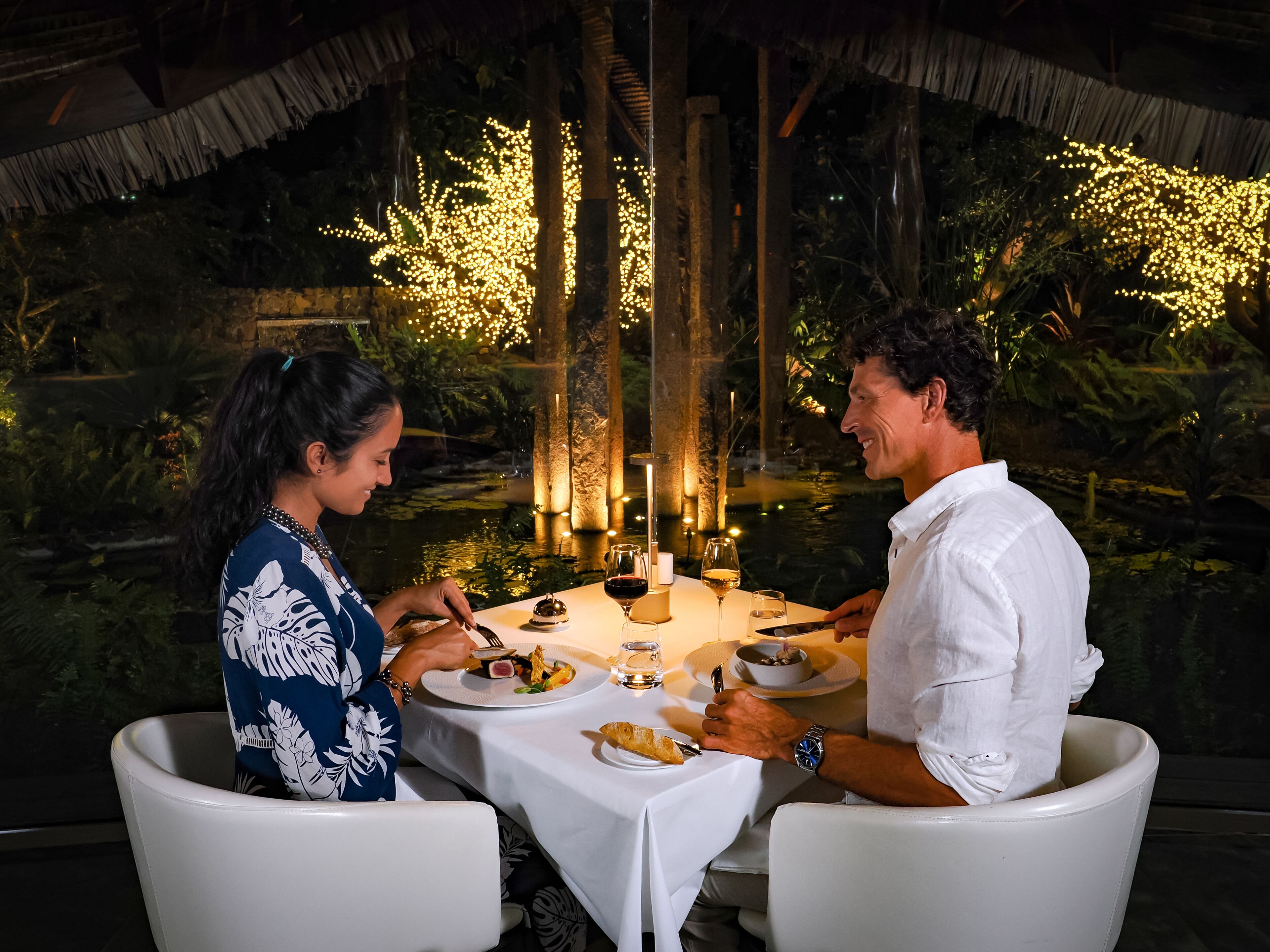 Una mesa de comedor al aire libre con velas, una copa de vino y platos de comida.