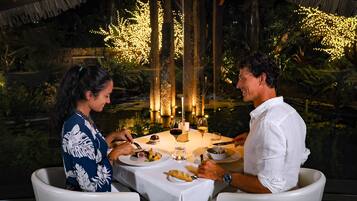 Una mesa de comedor al aire libre con velas, una copa de vino y platos de comida.