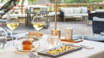 Un espace de restauration en plein air avec une table dressée pour deux personnes, comprenant un dessert, deux verres de vin blanc, un muffin et une bougie.