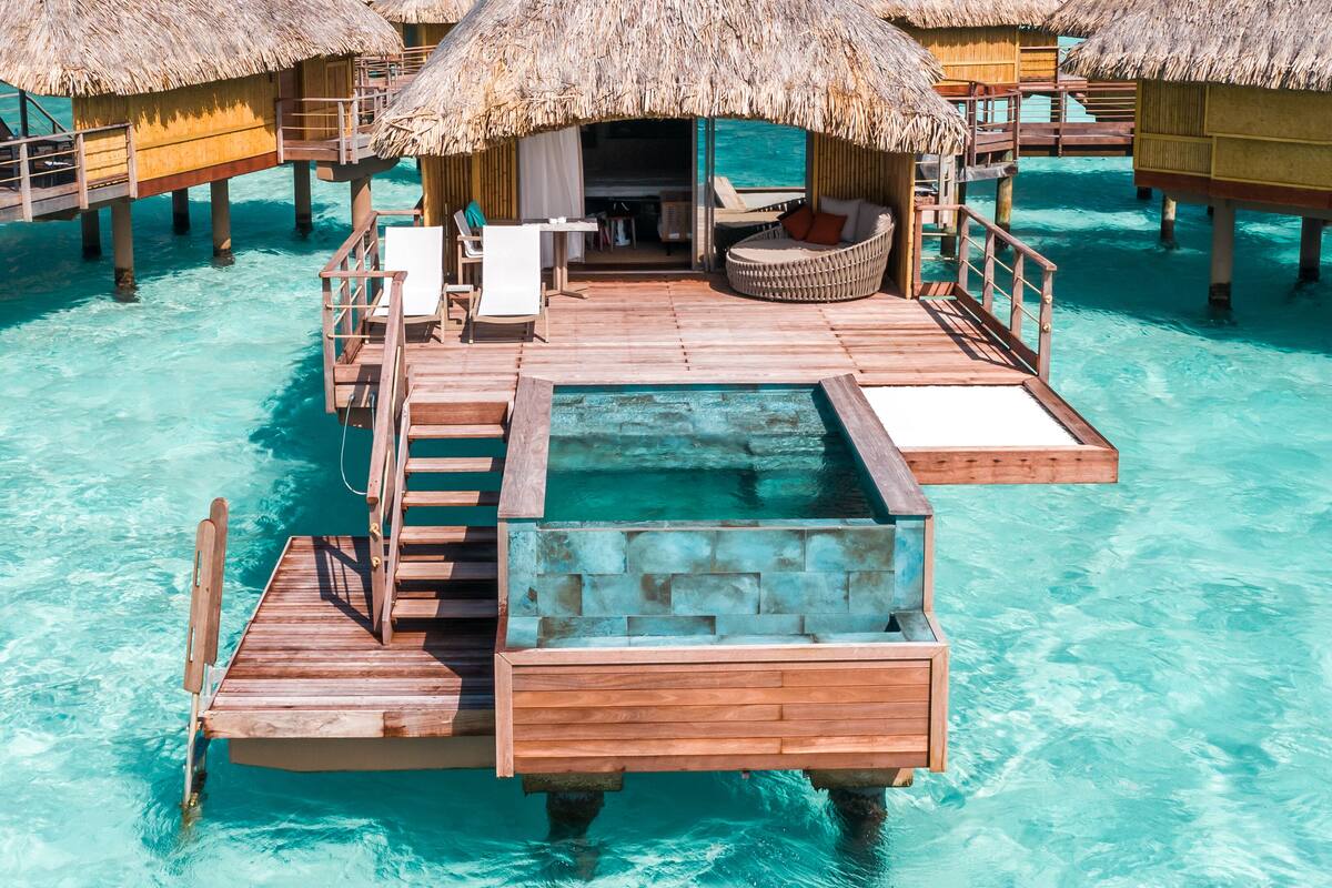 Bungalow sull'acqua con tetti di paglia, passerelle in legno e acque turchesi cristalline.