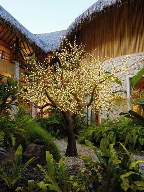 A tree with illuminated flowers in a garden area with thatched-roof buildings.