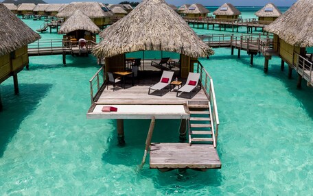 An overwater bungalows with thatched roofs, wooden deck, and lounge chairs.
