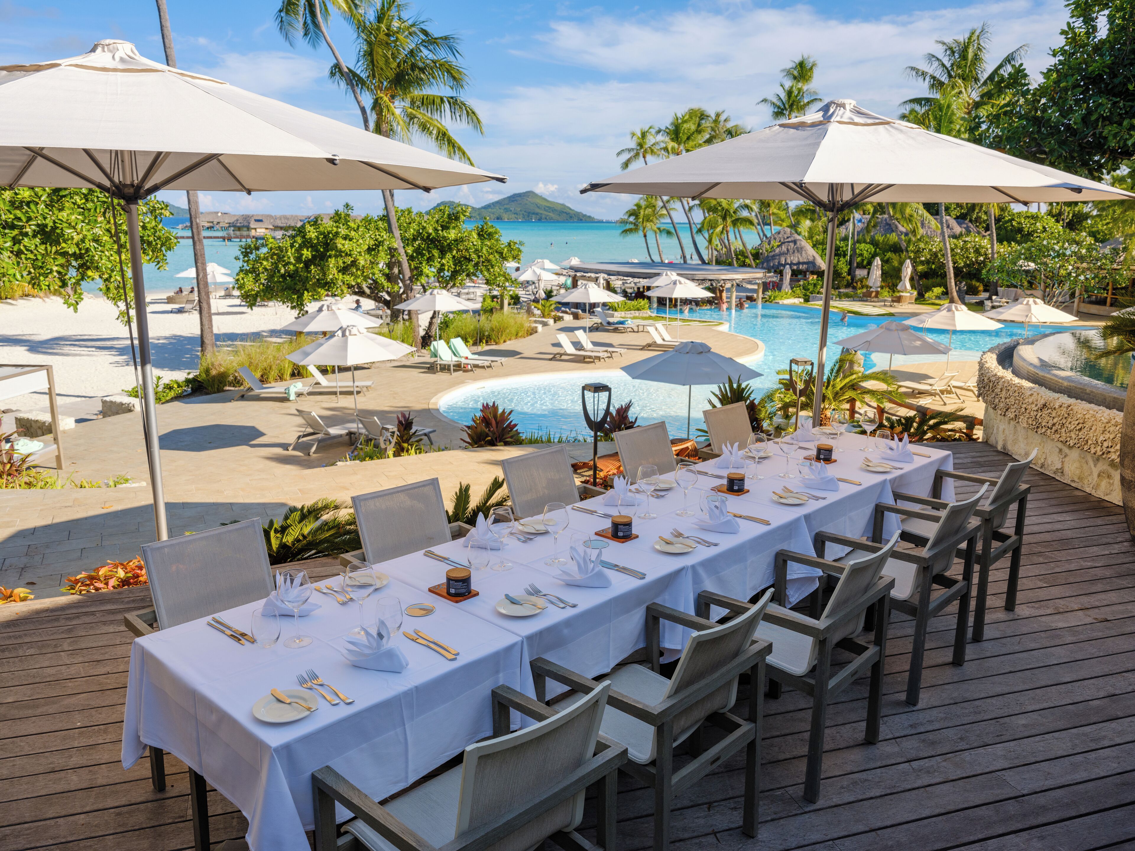 Un comedor con vistas a una piscina y playa, rodeado de palmeras y sombrillas.