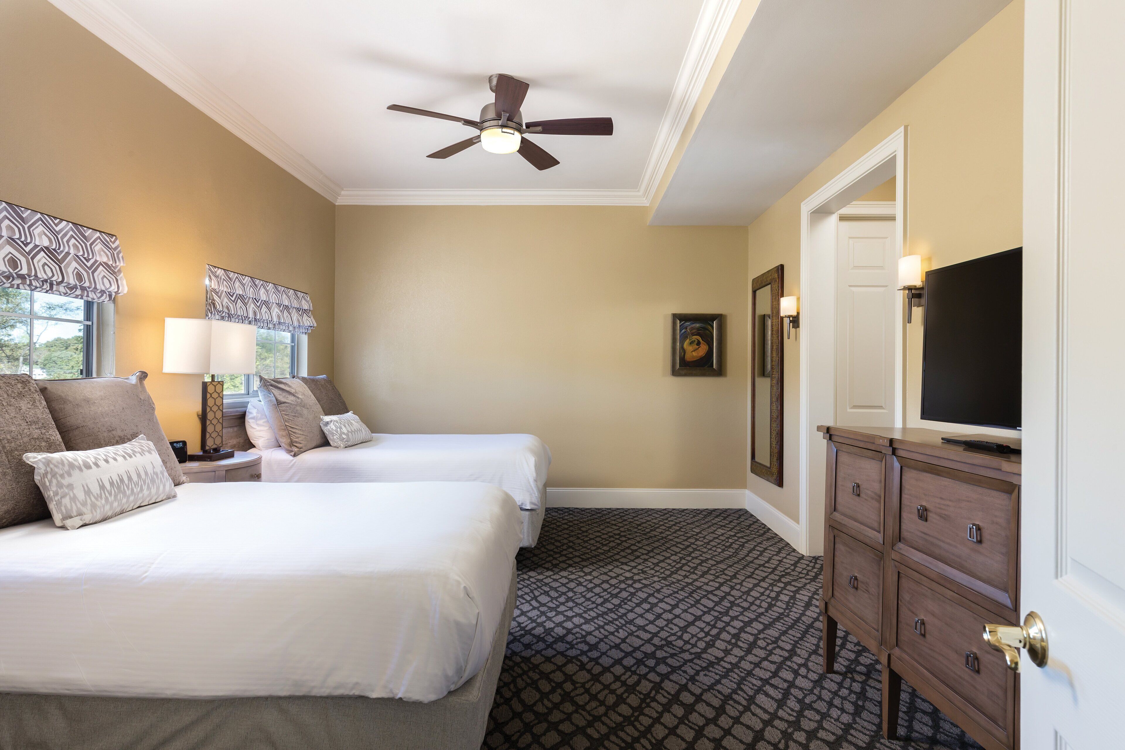 A hotel room with two beds, a ceiling fan, a dresser, and a television.