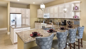 A modern kitchen with granite countertops, white cabinetry, and a central island with bar stools. - Club Wyndham Nashville (Nashville)