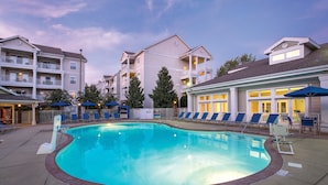 A swimming pool with lounge chairs and umbrellas, surrounded by multi-story buildings with balconies. - Club Wyndham Nashville (Nashville)