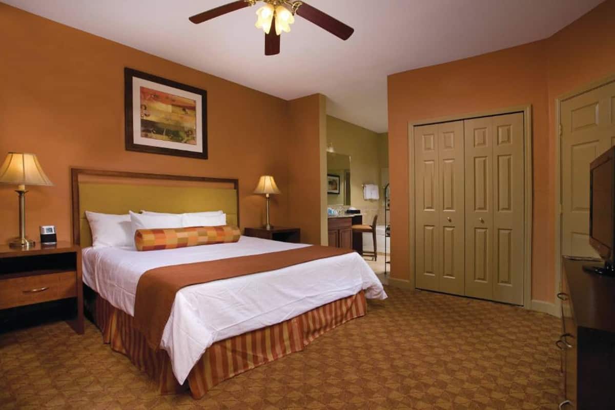 A hotel room with a large bed, two bedside tables with lamps, a ceiling fan, and a wardrobe.