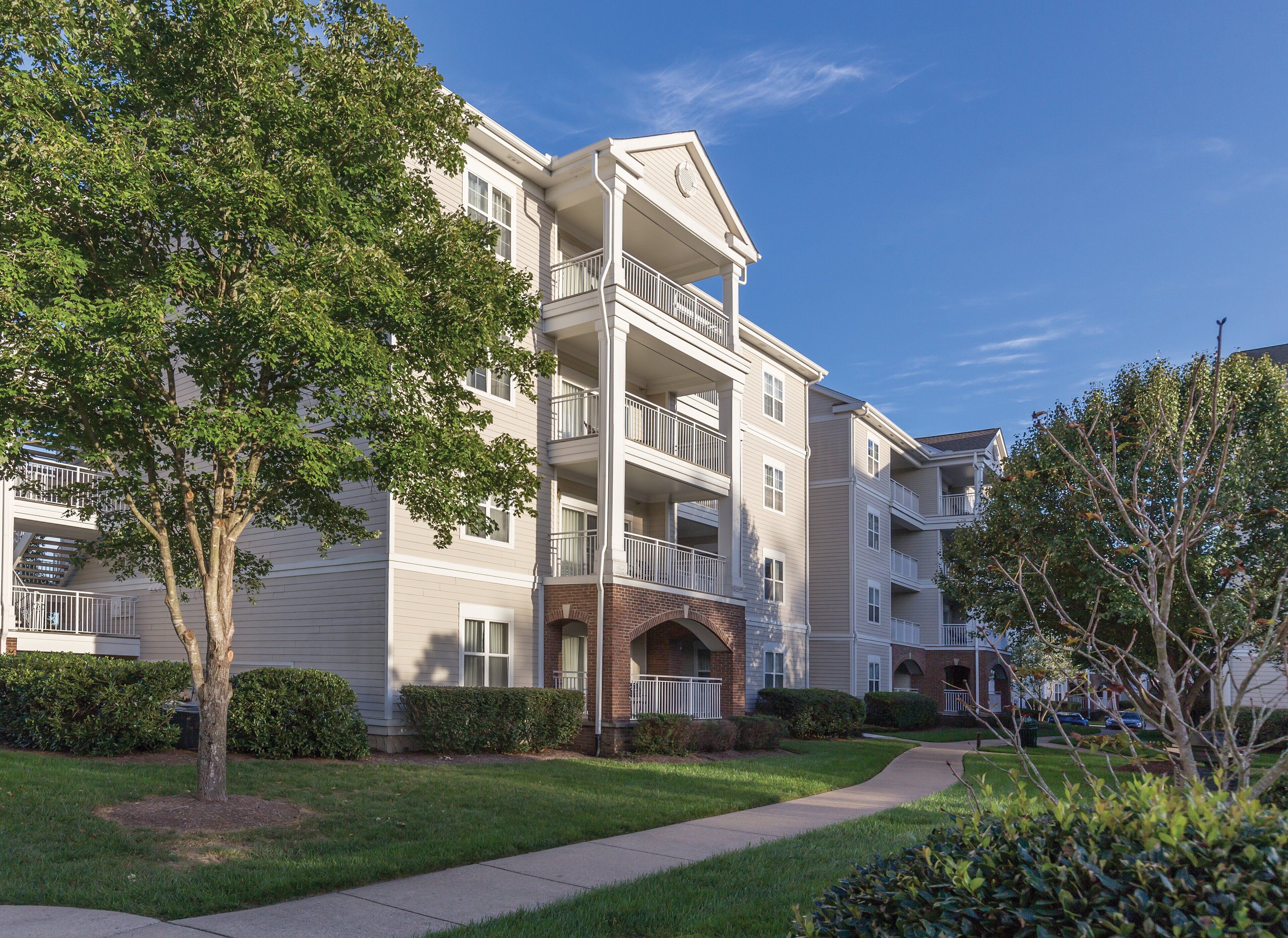A multi-story residential building with balconies, a brick entrance, and a well-maintained lawn.