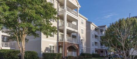 A multi-story residential building with balconies, a brick entrance, and a well-maintained lawn.