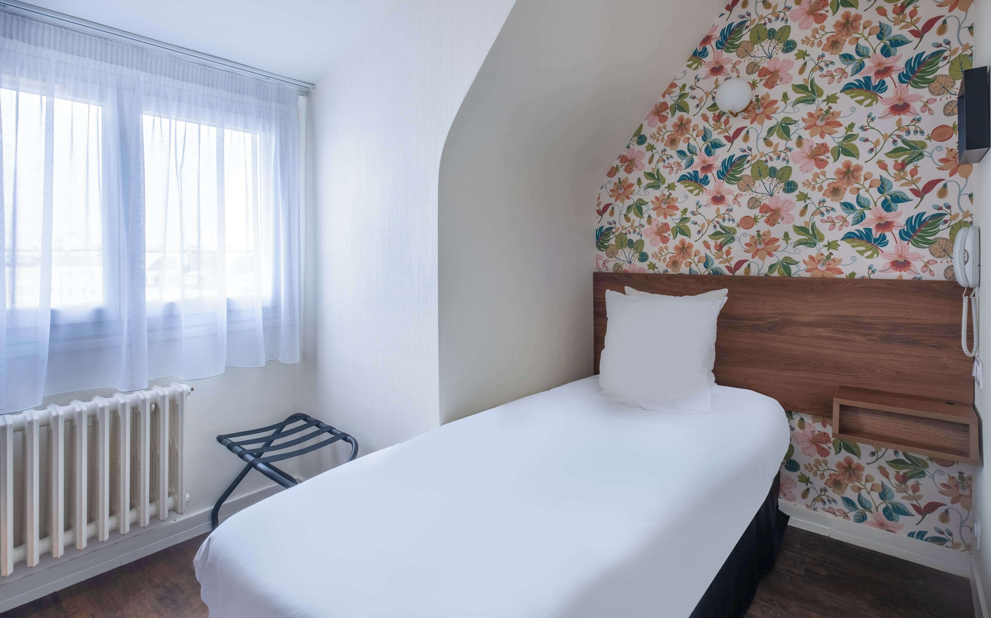 A single bed with a wooden headboard in a room with a floral wallpaper pattern.