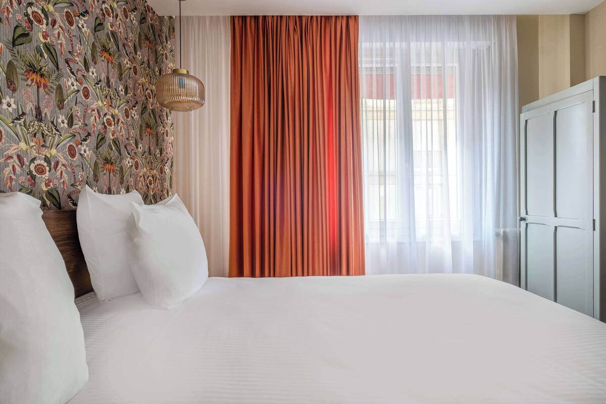 Ein Hotelzimmer mit einem großen Bett, einem hölzernen Kopfteil und einer Wand mit floralem Muster.
