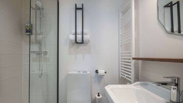 A modern bathroom with a glass-enclosed shower, a white toilet, and a sink with a mirror above it.