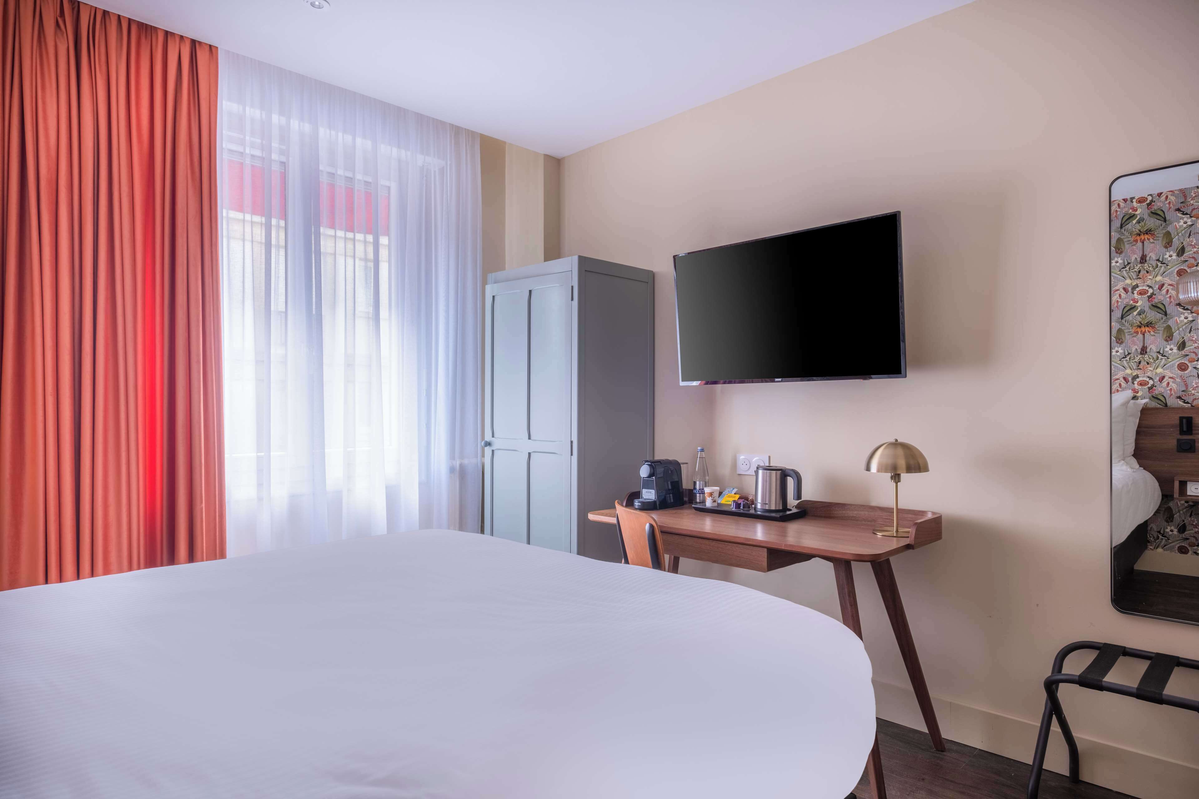 Habitació d'hotel amb un llit gran, una taula amb una cafetera, un televisor i un armari.