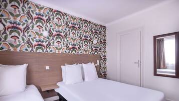 A hotel room with two beds, a patterned wallpaper, a wooden headboard, a bedside table, and a window with curtains.