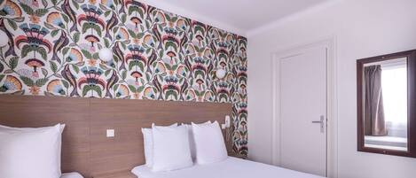 A hotel room with two beds, a patterned wallpaper, a wooden headboard, a bedside table, and a window with curtains.