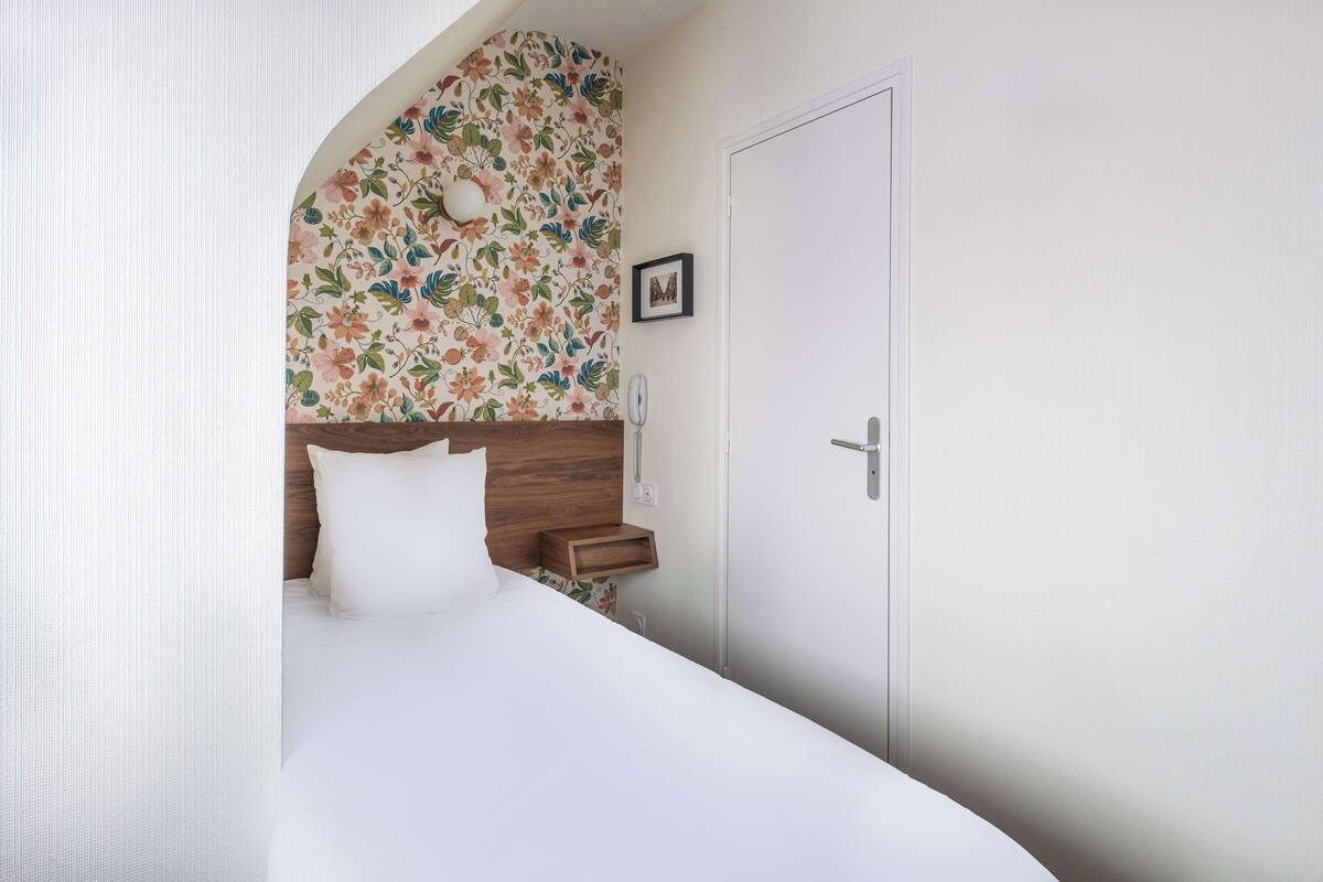 Ein Schlafzimmer mit Bett, Holz-Kopfteil, Nachttisch, einer Tür und einer Wand mit Blumenmuster.