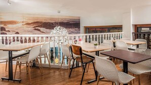 Un restaurante con mesas y sillas de madera, un amplio mural marino y un balcón con barandilla.