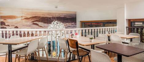 A restaurant with wooden tables and chairs, a large ocean mural, and a balcony with a railing.