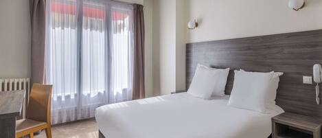 A hotel room with a large bed, a wooden nightstand, a desk, and a chair.