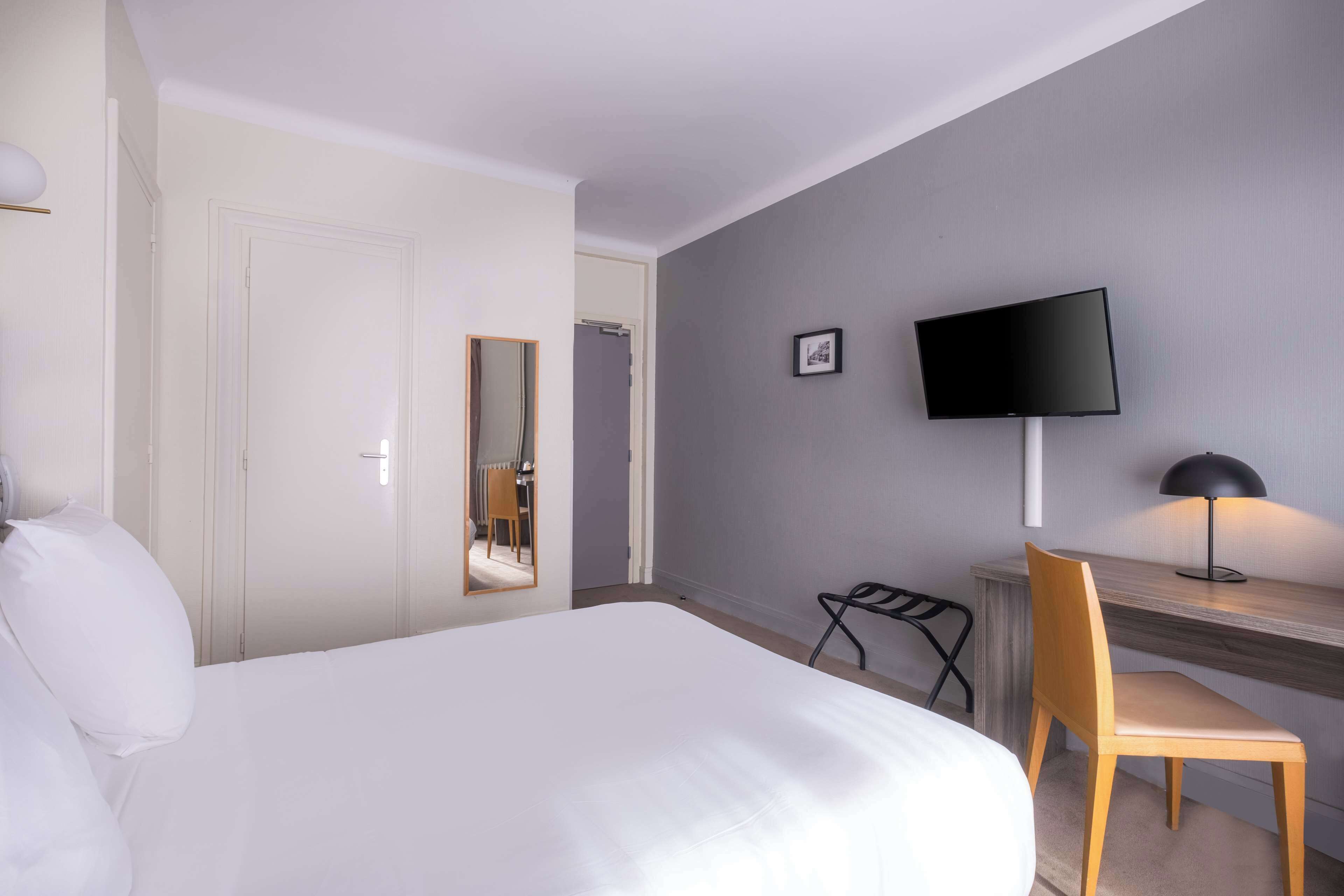 Une chambre d’hôtel comprenant un lit, un bureau avec une chaise, une télévision et un miroir.