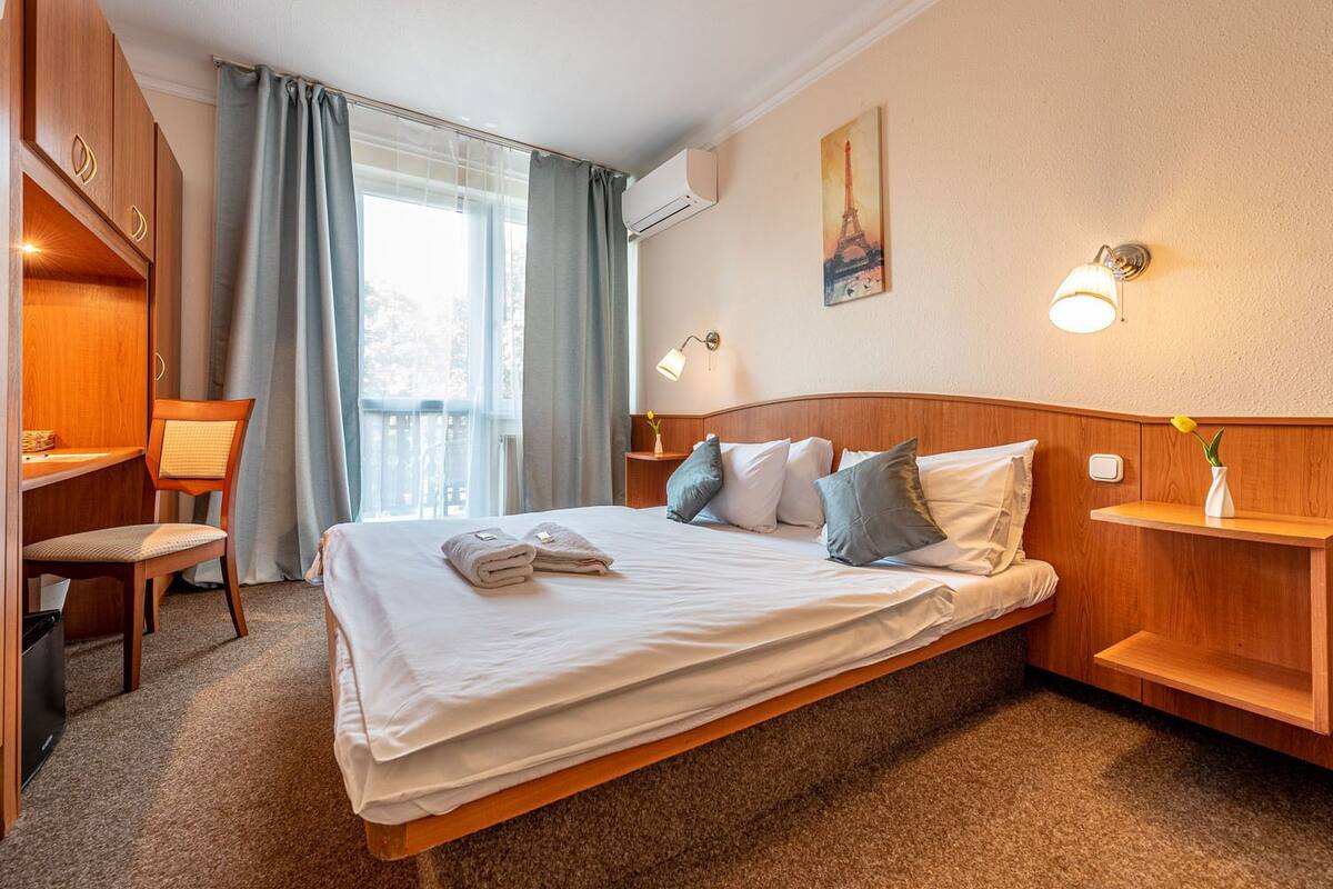 Habitación de hotel con cama, escritorio, silla, mesita de noche y un cuadro de la Torre Eiffel.